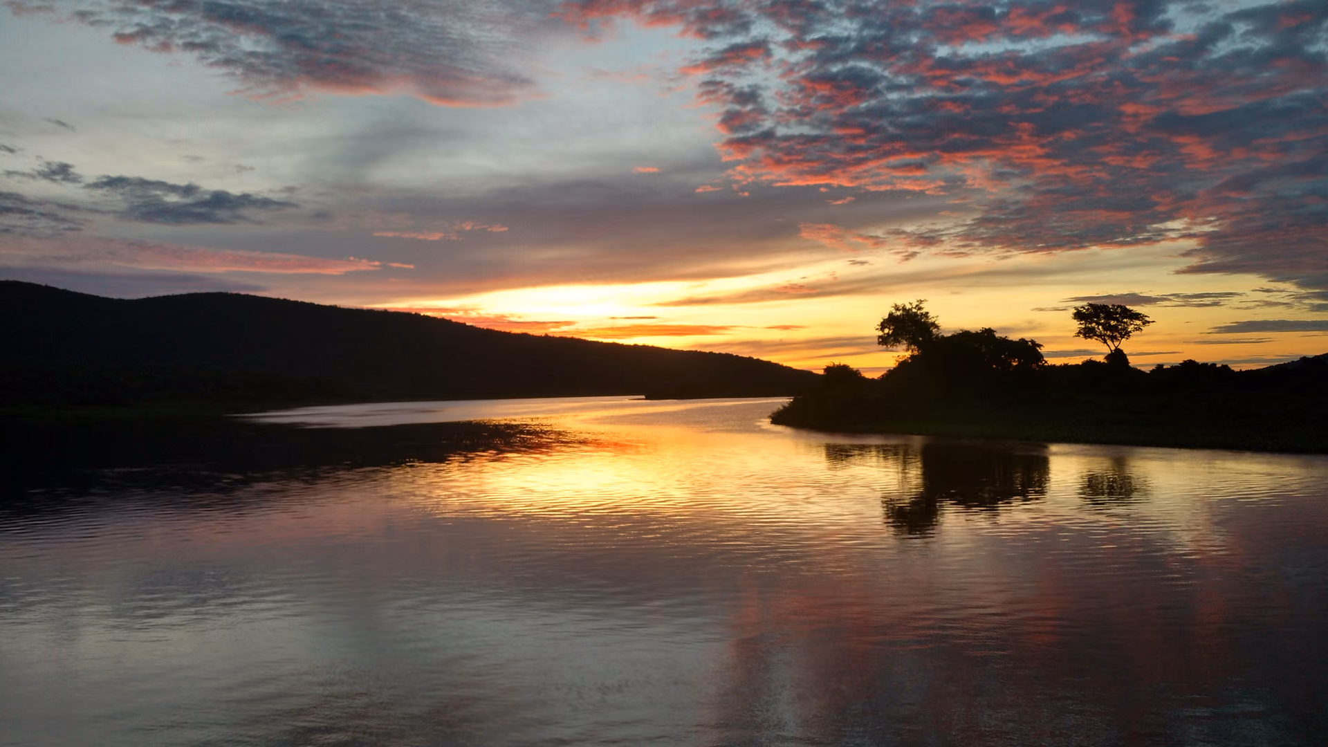 Entardecer no rio Paraguai, no Pantanal: céu laranja e rosa refletido na água, com a silhueta das árvores na margem